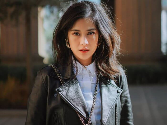 Dian Sastro menggunakan kemeja putih dan jaket leather hitam memandang ke kamera